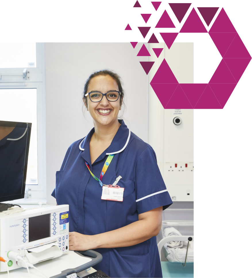 A smiling nurse in blue scrubs and glasses, wearing an id badge, stands beside medical equipment in a hospital room. a stylized pink geometric shape overlays part of the image.