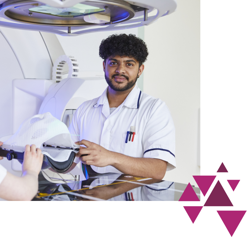 Male healthcare professional in a white uniform adjusts equipment in a high-tech medical setup, looking at the camera, with radiology machinery in the background.