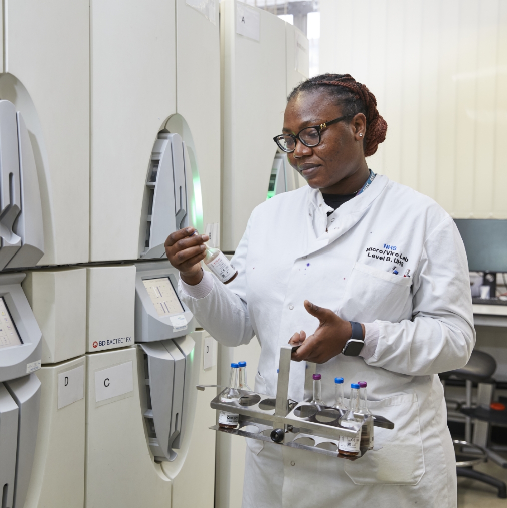 A female scientist in a lab coat and glasses conducts an experiment using an analytical machine in a laboratory, handling samples in test tubes.